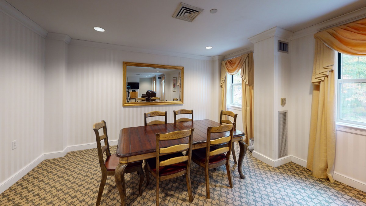 A traditional dining room with a wooden table and chairs, decorated with a large mirror and draped curtains.
