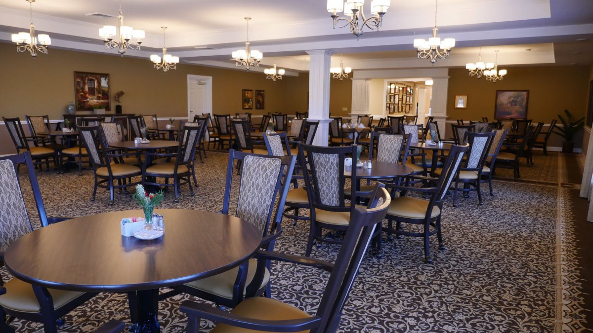An empty dining area with neatly arranged tables and chairs, featuring elegant decor and lighting.