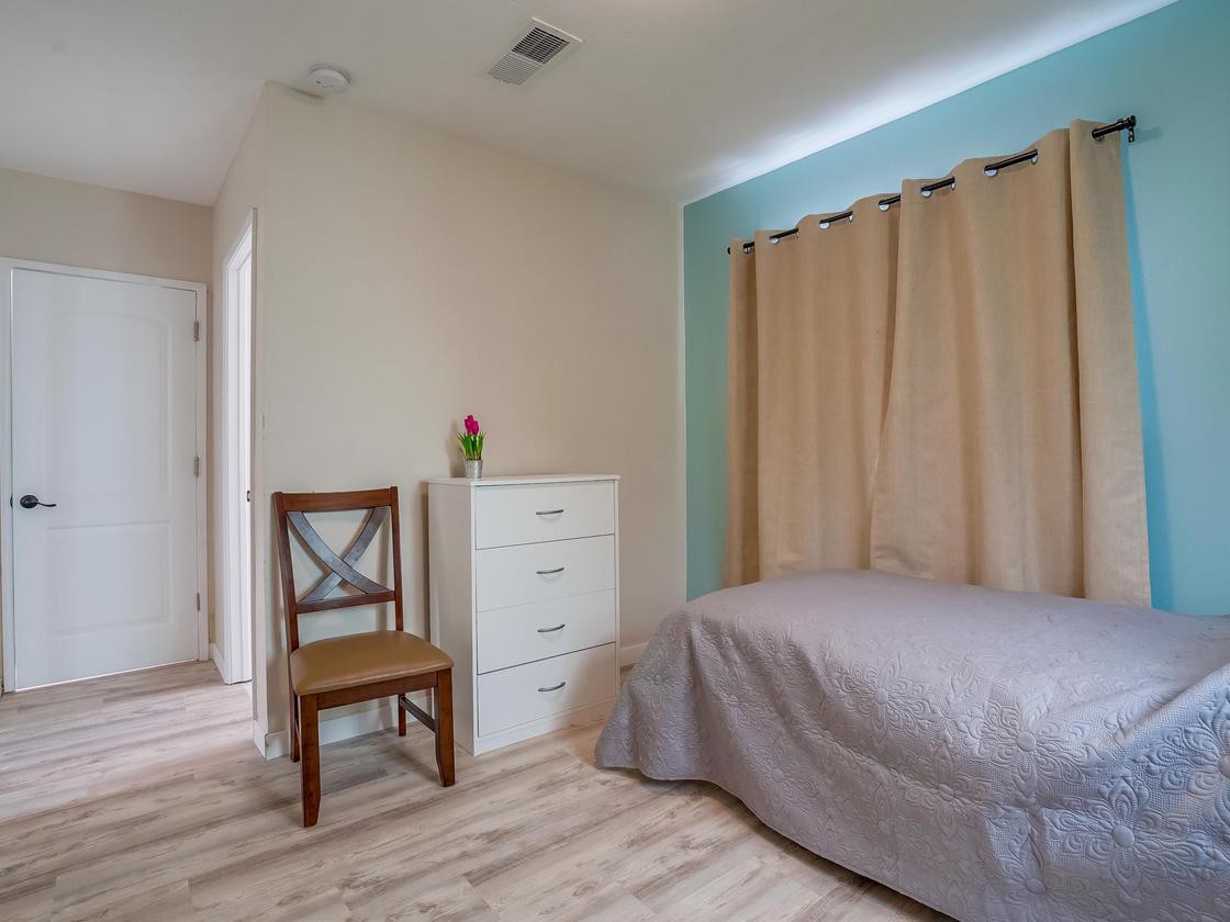 A minimalist bedroom with a single bed, dresser, and chair.