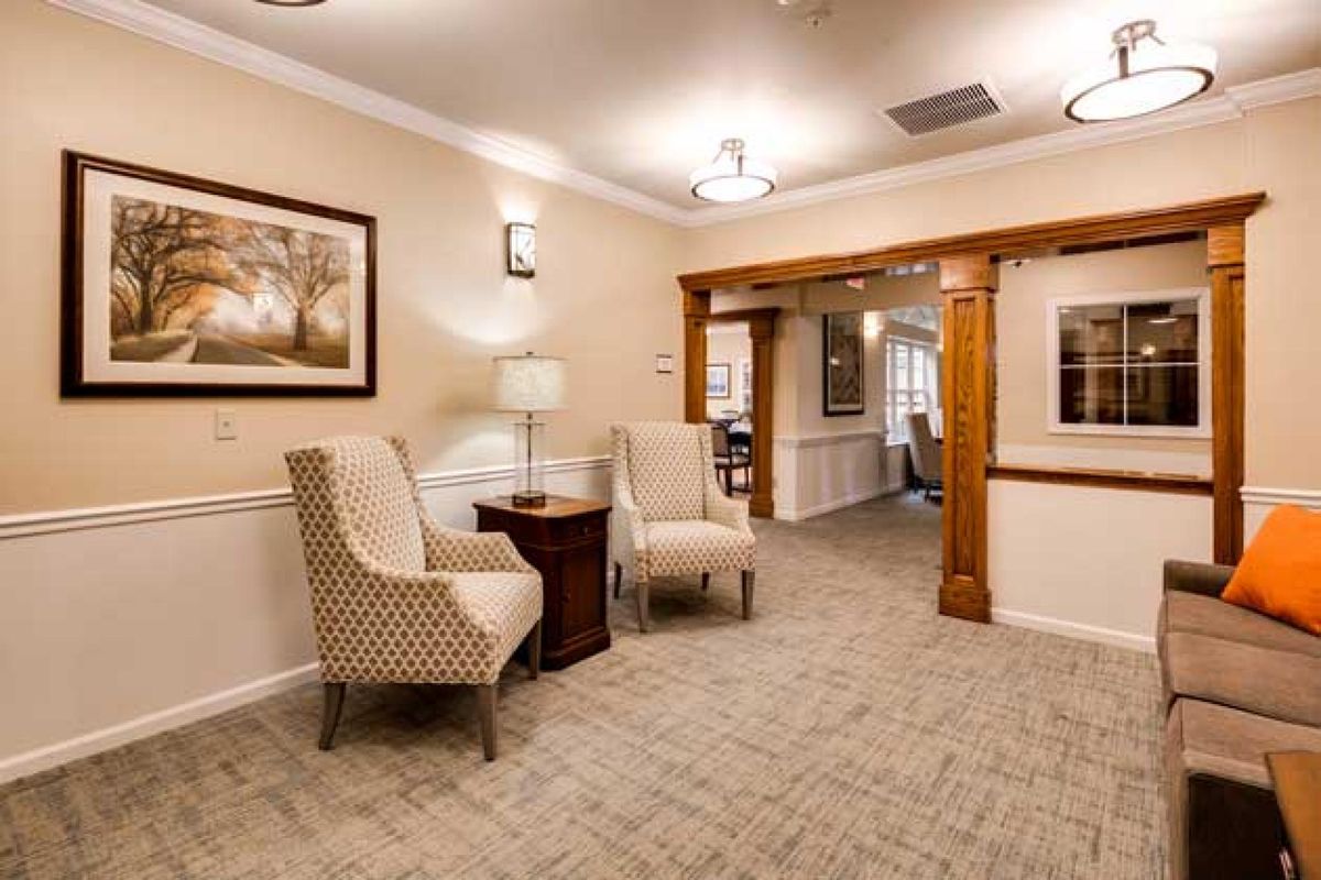 A cozy living area featuring comfortable chairs, a side table with a lamp, and framed artwork on the walls.