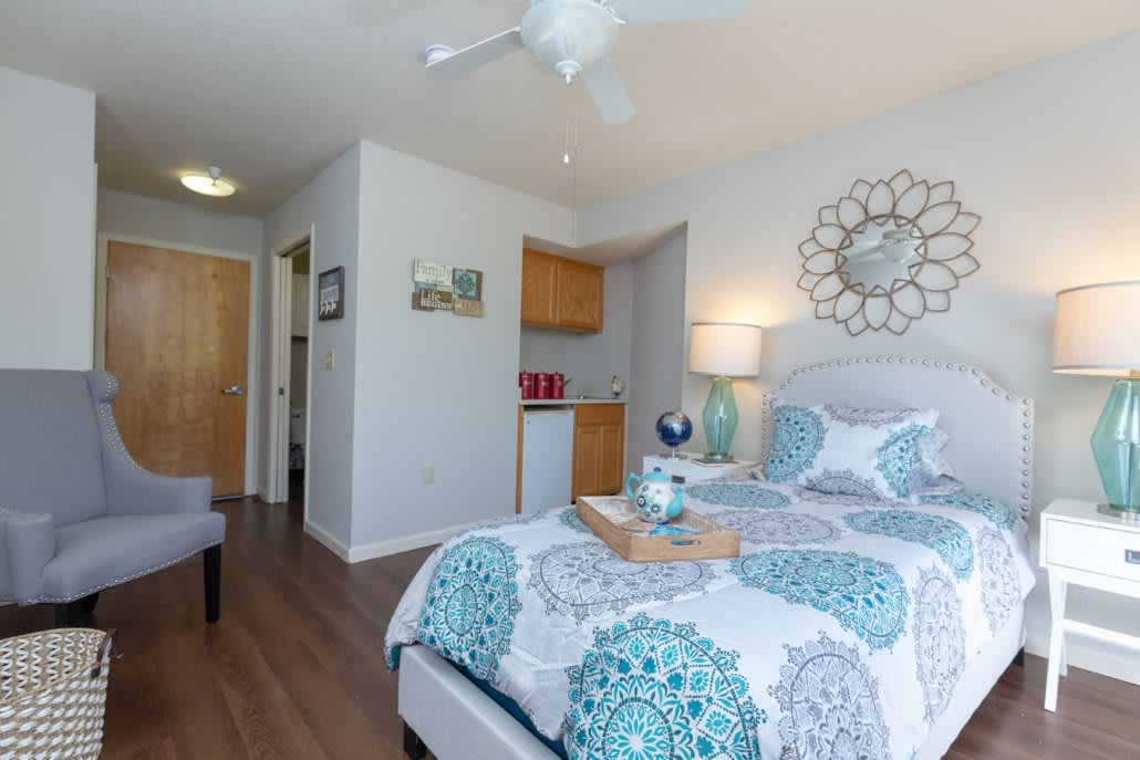 A cozy and well-decorated bedroom with a stylish bedspread, decorative mirror, and wooden floor.