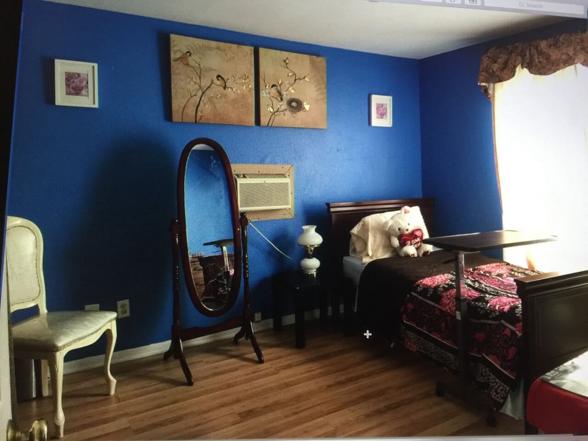 A cozy bedroom with blue walls, featuring a decorative mirror, artwork, and natural light streaming through the window.