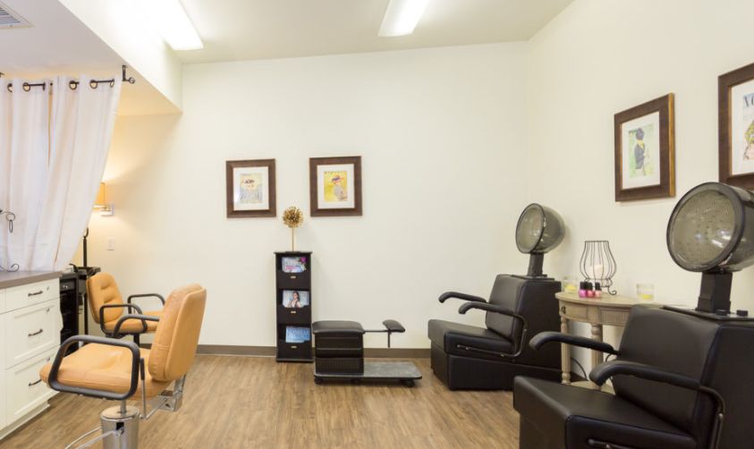 The image shows a hair salon interior with chairs and decor, featuring a waiting area and wooden flooring.