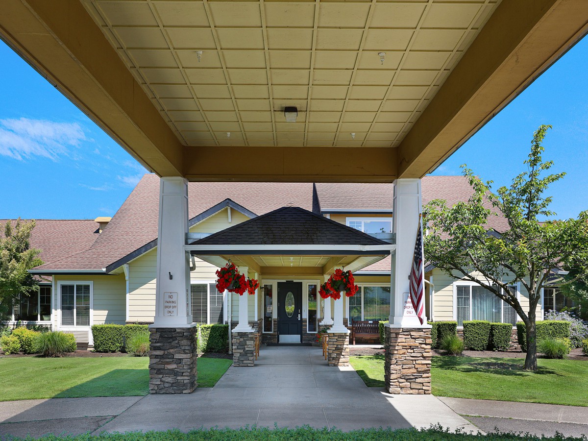 A view of a residential building with a covered entrance and landscaped surroundings.