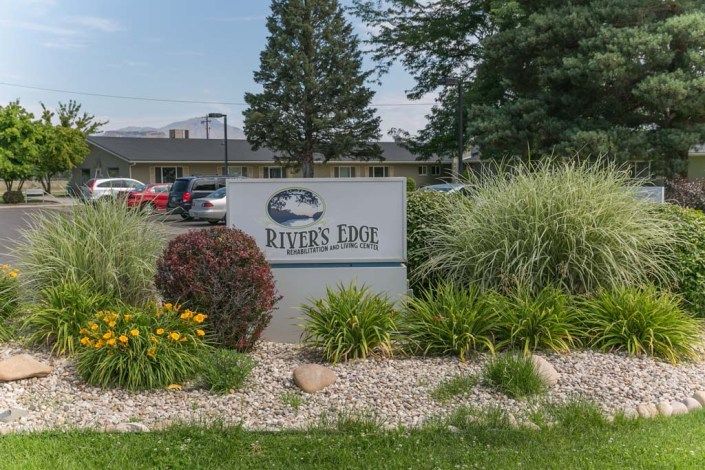 A sign for River's Edge amidst landscaped greenery with a building in the background.