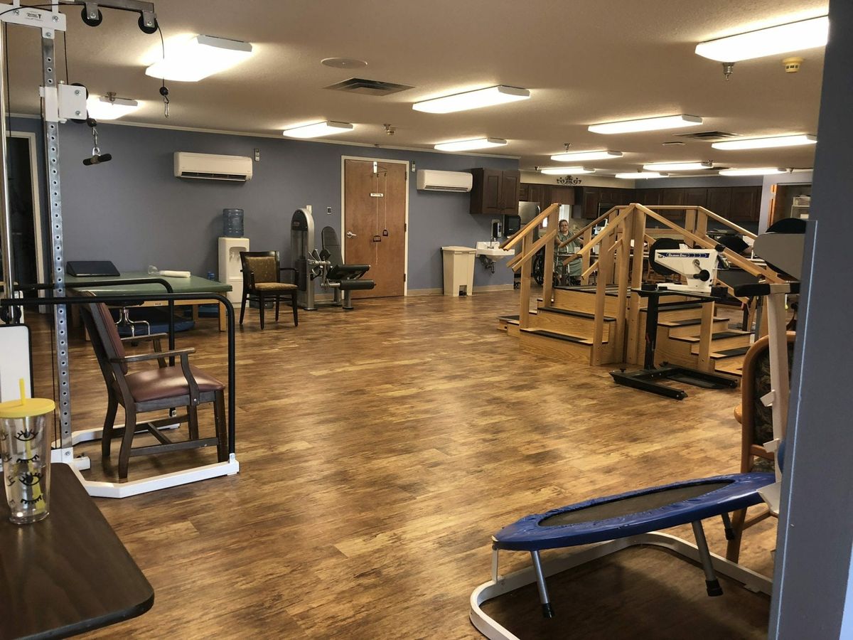 An empty gym with various exercise equipment and wooden flooring.