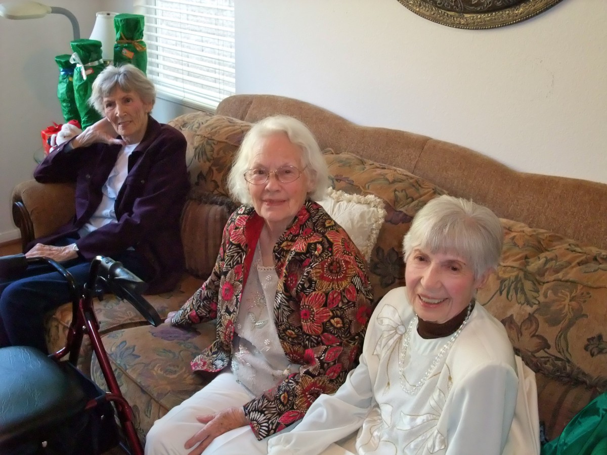 A group of senior women sitting together in a living room, smiling at the camera.