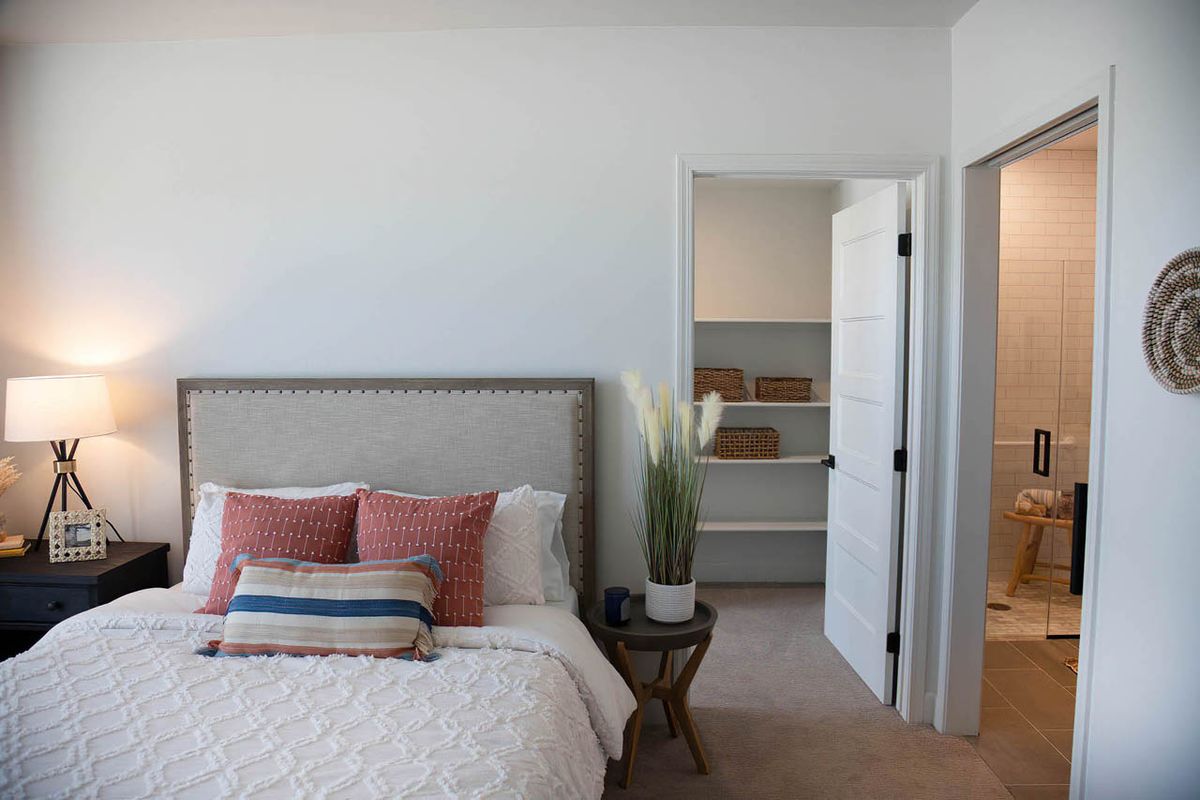 A modern, minimalist bedroom featuring a comfortable bed with decorative pillows and an open closet.
