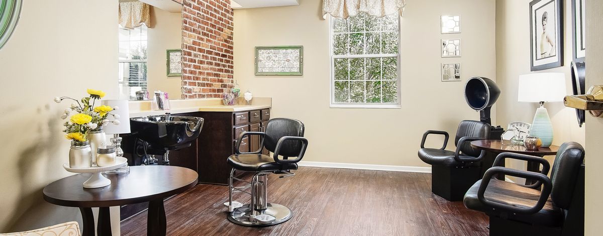 A spacious hair salon interior with a styling chair, mirror, and large window.
