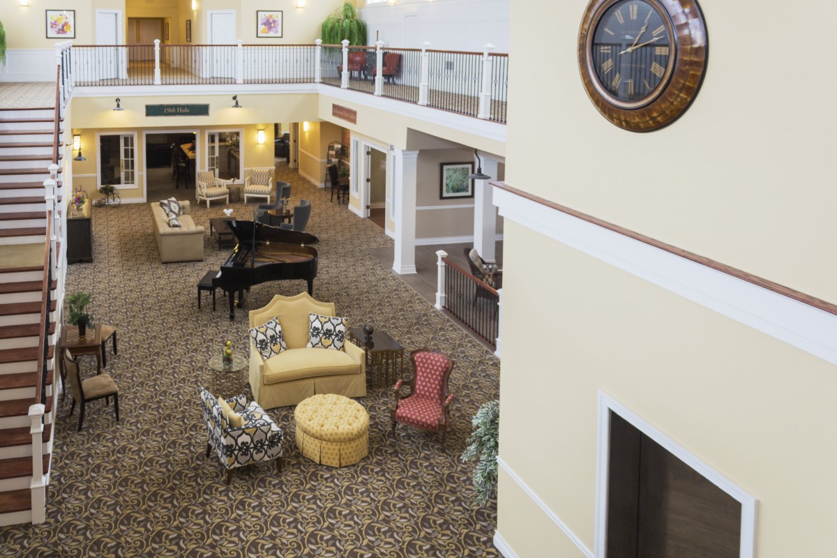A spacious lobby with seating arrangements, a grand piano, and a large wall clock in a two-story building.