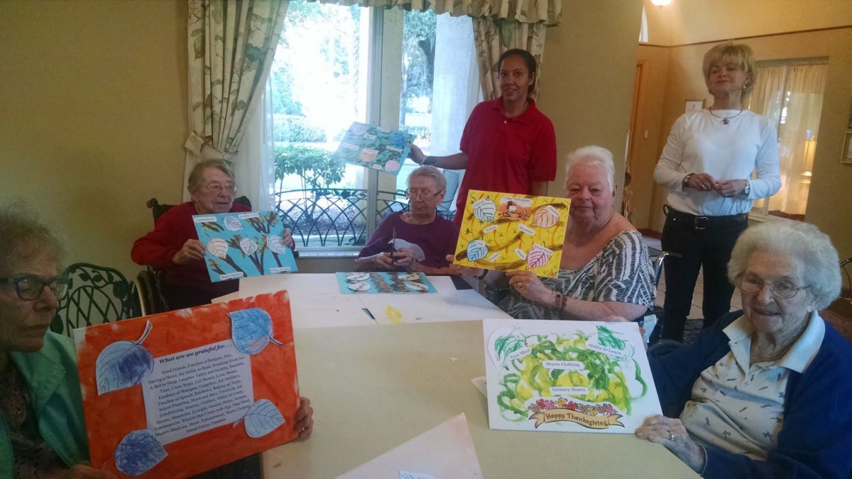 Elderly individuals proudly display their paintings during an art class at a nursing home.