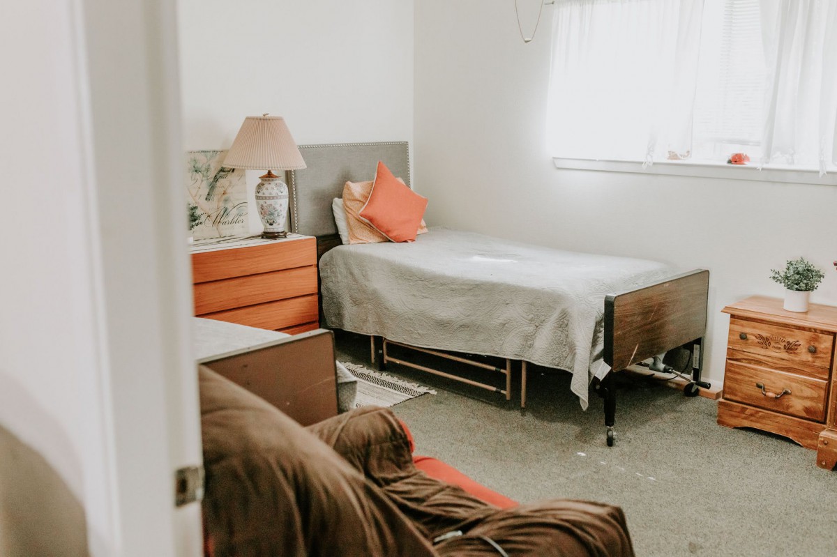 A cozy bedroom with a single bed, dresser, and lamp, highlighted by natural light.