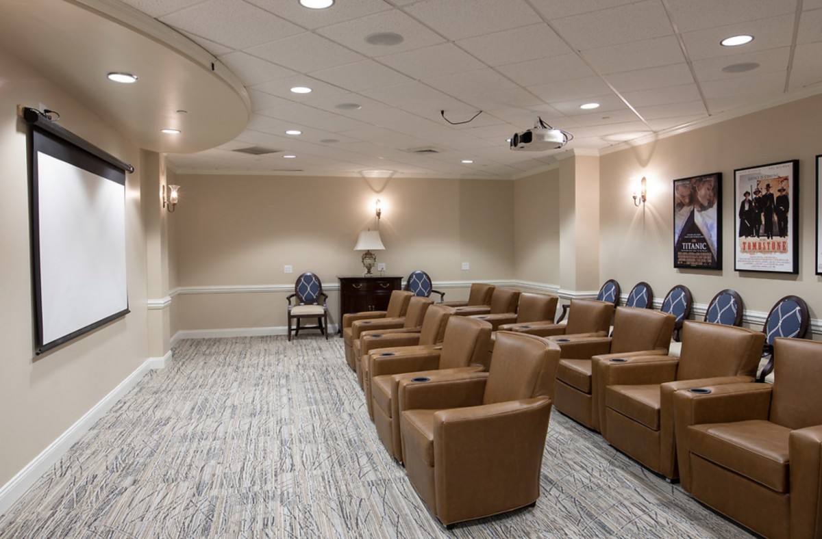 A cozy theater-style seating area with armchairs and a projector in a well-lit room.
