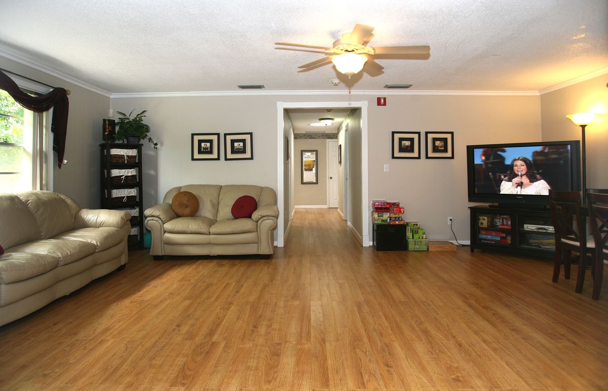 A cozy living room with hardwood flooring, featuring a sofa, television, and ceiling fan, leading into a hallway.
