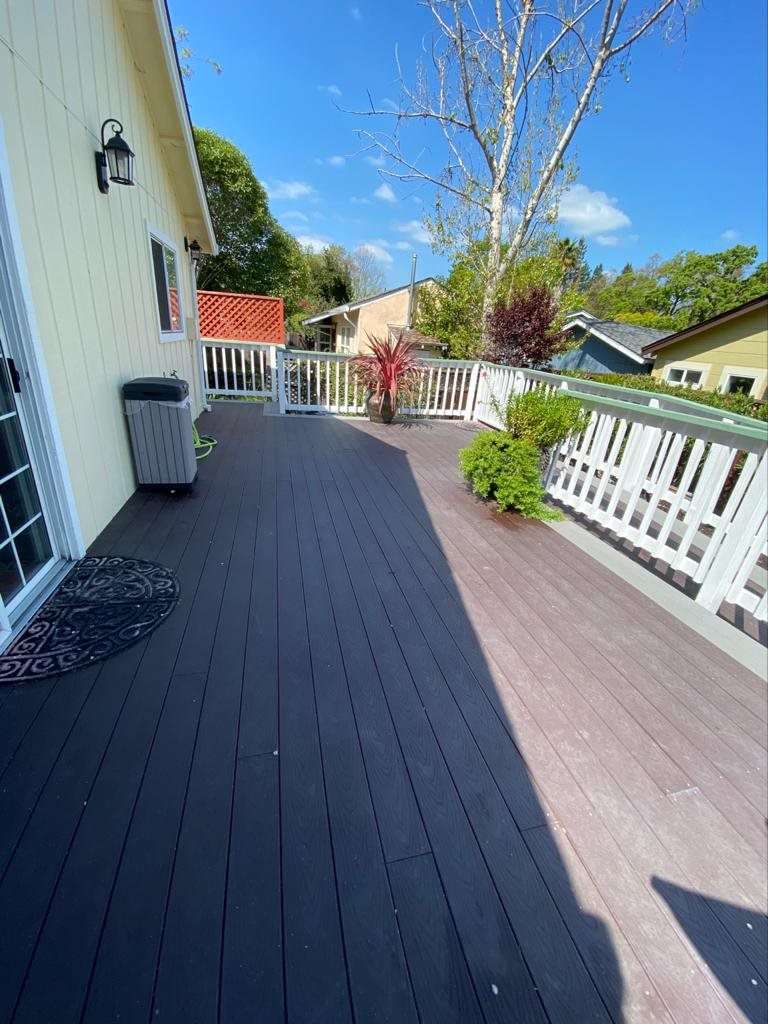 A sunny outdoor deck with a white fence and plants.
