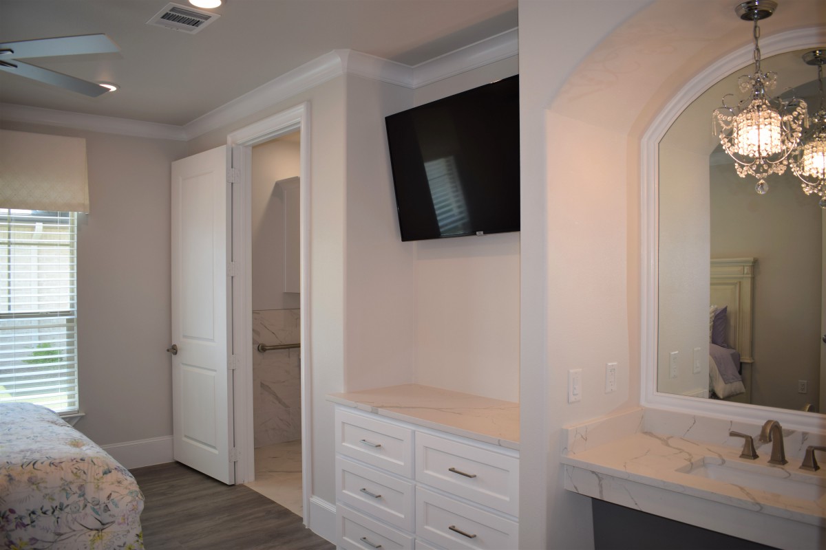Modern bedroom with a television mounted above a dresser and an adjacent vanity mirror.