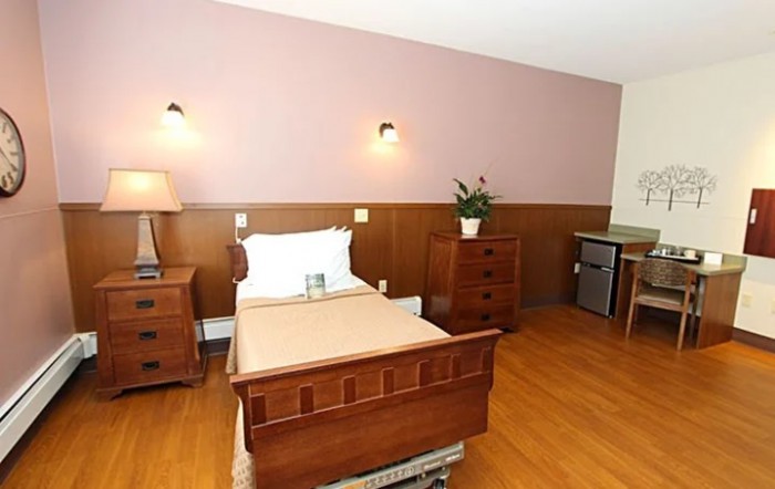A simple, well-furnished hospital room with a wooden single bed and matching furniture.