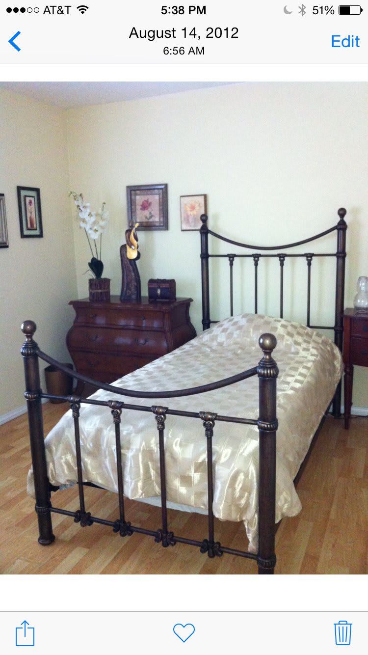 A cozy bedroom with a single metal-framed bed, wooden dresser, and decorative items on display.