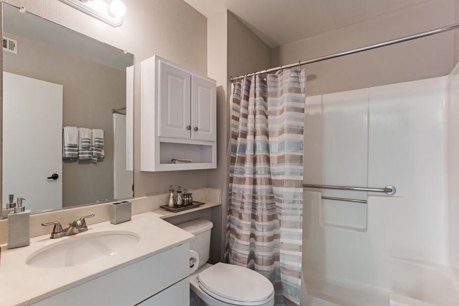 A modern bathroom with a shower curtain, sink, and storage cabinet.