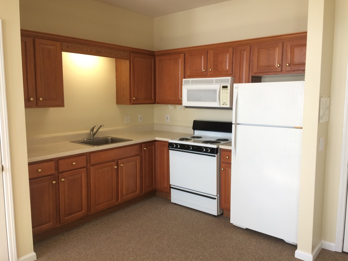 A kitchen with wooden cabinets, featuring a refrigerator, microwave, stove, and sink.
