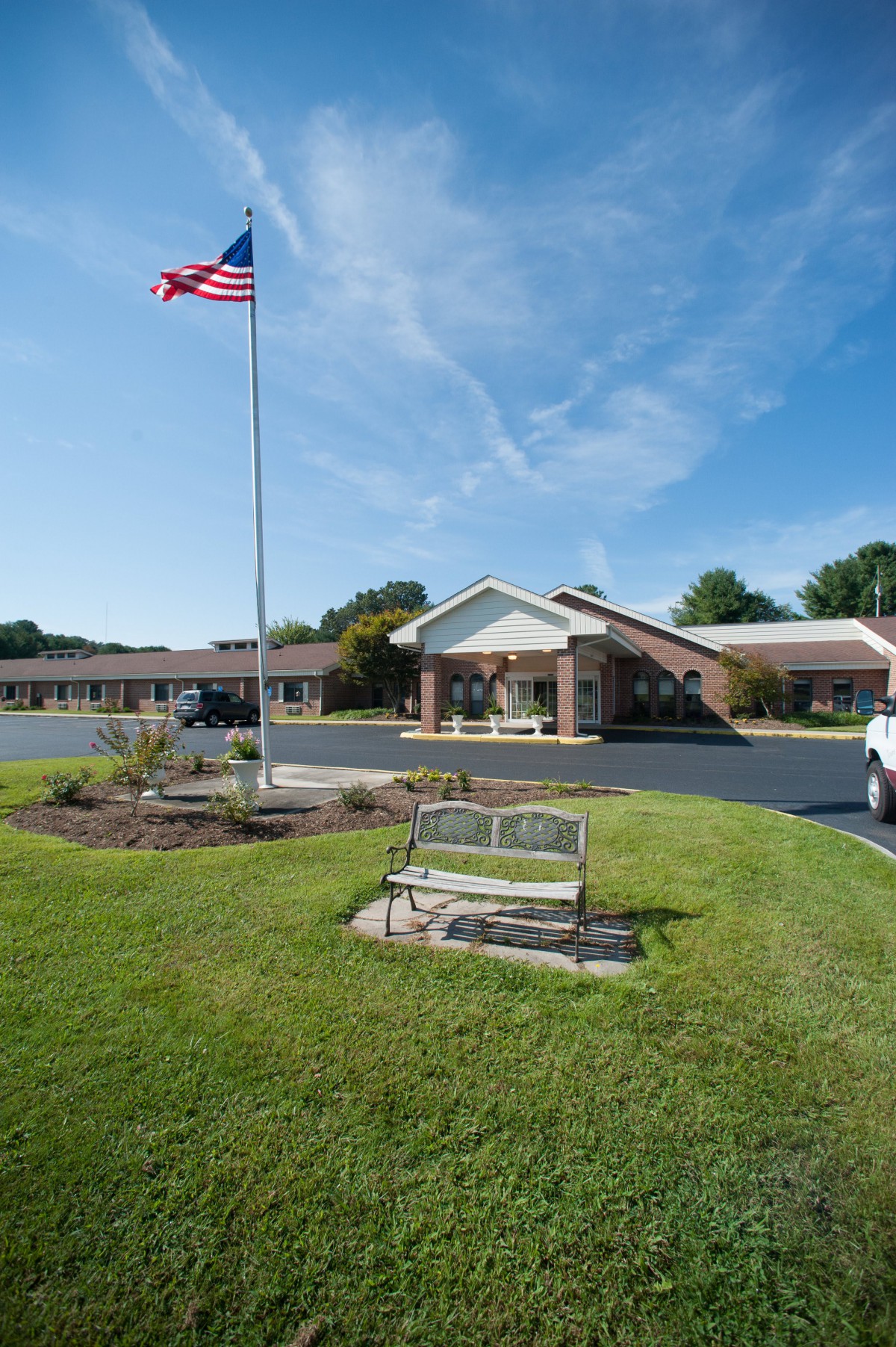 A motel with an American flag and neatly landscaped grounds, featuring a bench in the front.