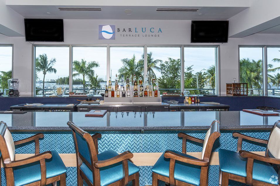 A modern bar interior with views of palm trees through large windows.