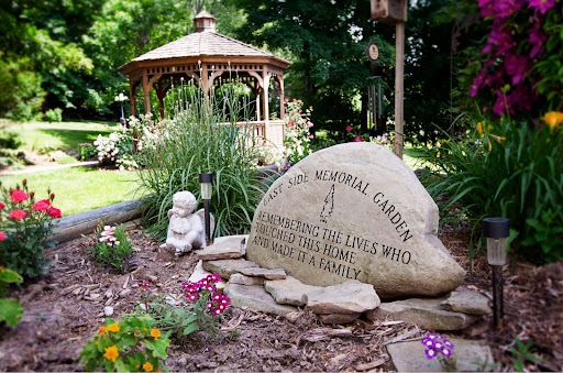 A serene memorial garden featuring a gazebo, vibrant flowers, and a stone monument honoring beloved pets.