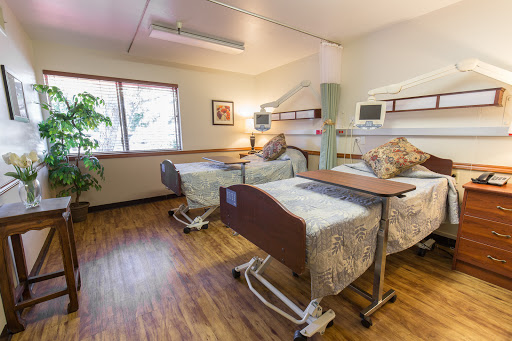A cozy hospital patient room featuring two adjustable beds and natural light from a nearby window.
