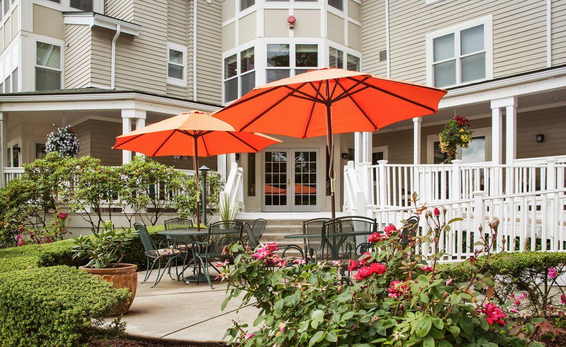 A cozy patio area with bright orange umbrellas and lush flower beds in front of a residential building.
