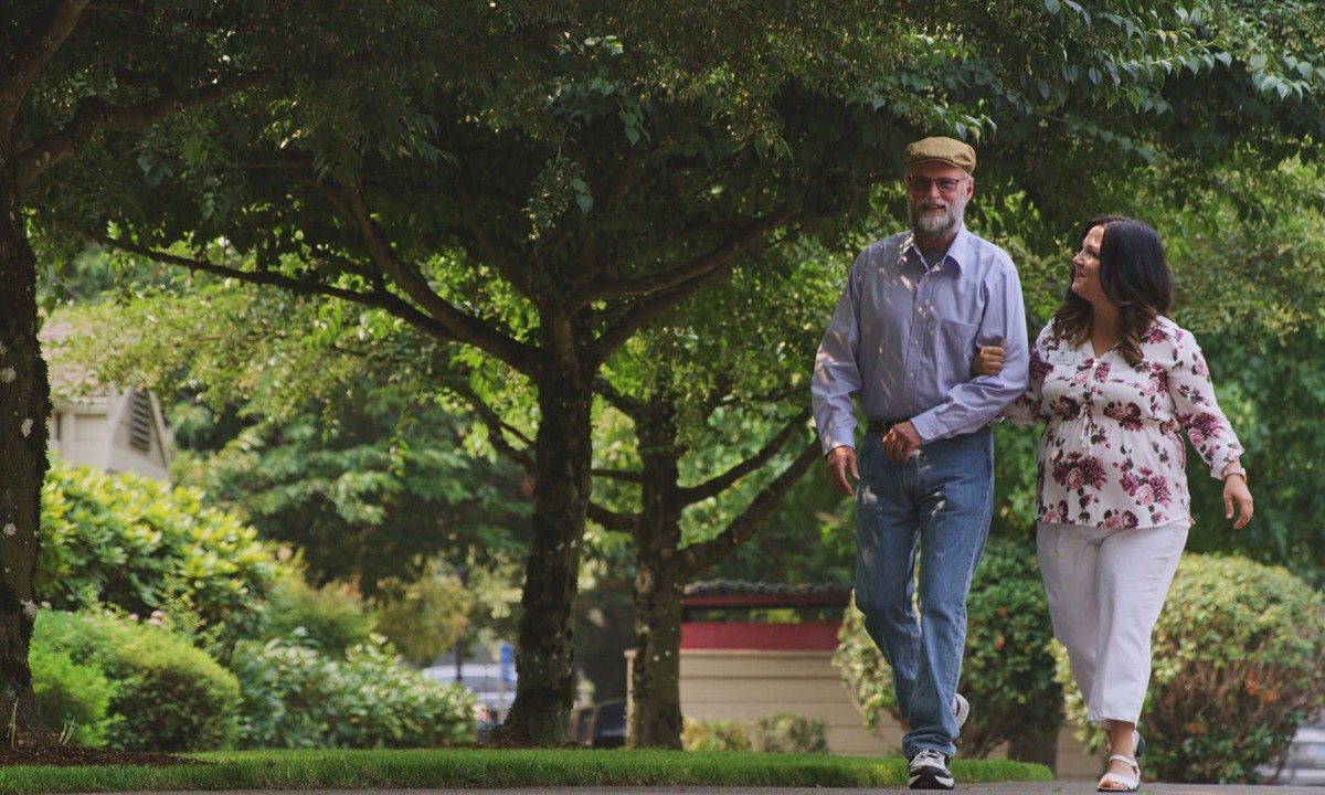 Two people walking in a park surrounded by trees.