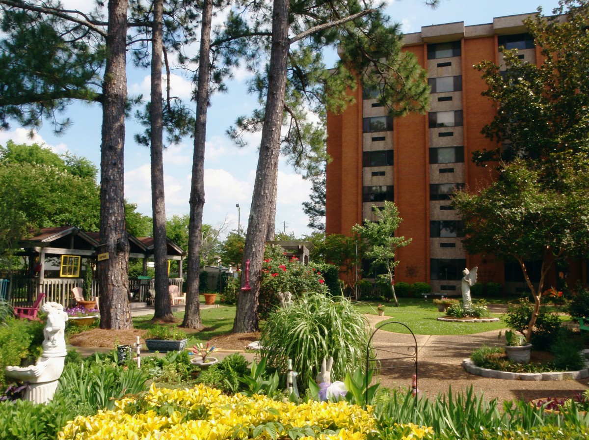 A tranquil garden area with tall trees and colorful flowers next to an apartment building.