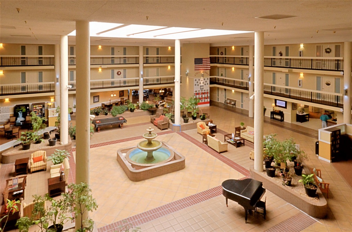 Spacious hotel atrium with a fountain and grand piano, surrounded by indoor plants and elegant seating areas.