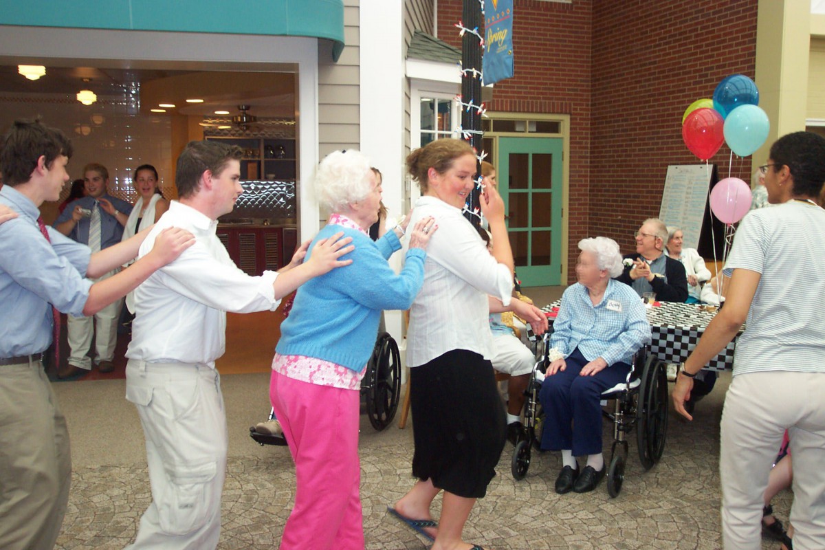A group of people enjoying a conga line dance indoors, with seniors participating in the fun.