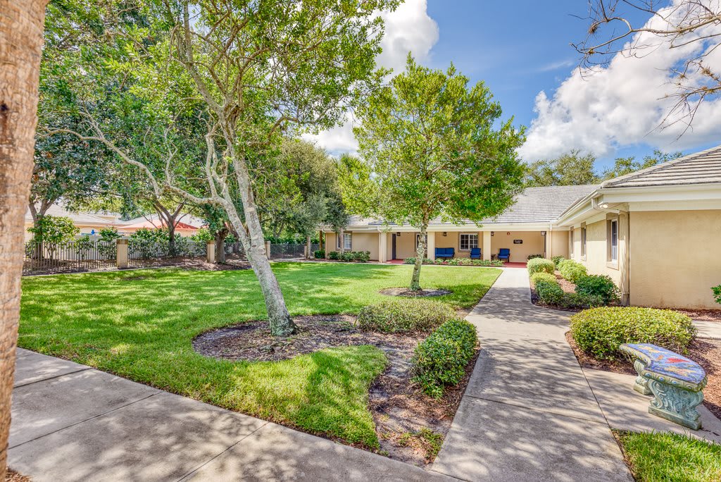 A beautifully landscaped garden with a lush green lawn and well-maintained trees lining a paved pathway.