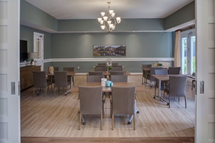 A formal dining room with multiple tables and chairs, featuring a chandelier and wooden flooring.