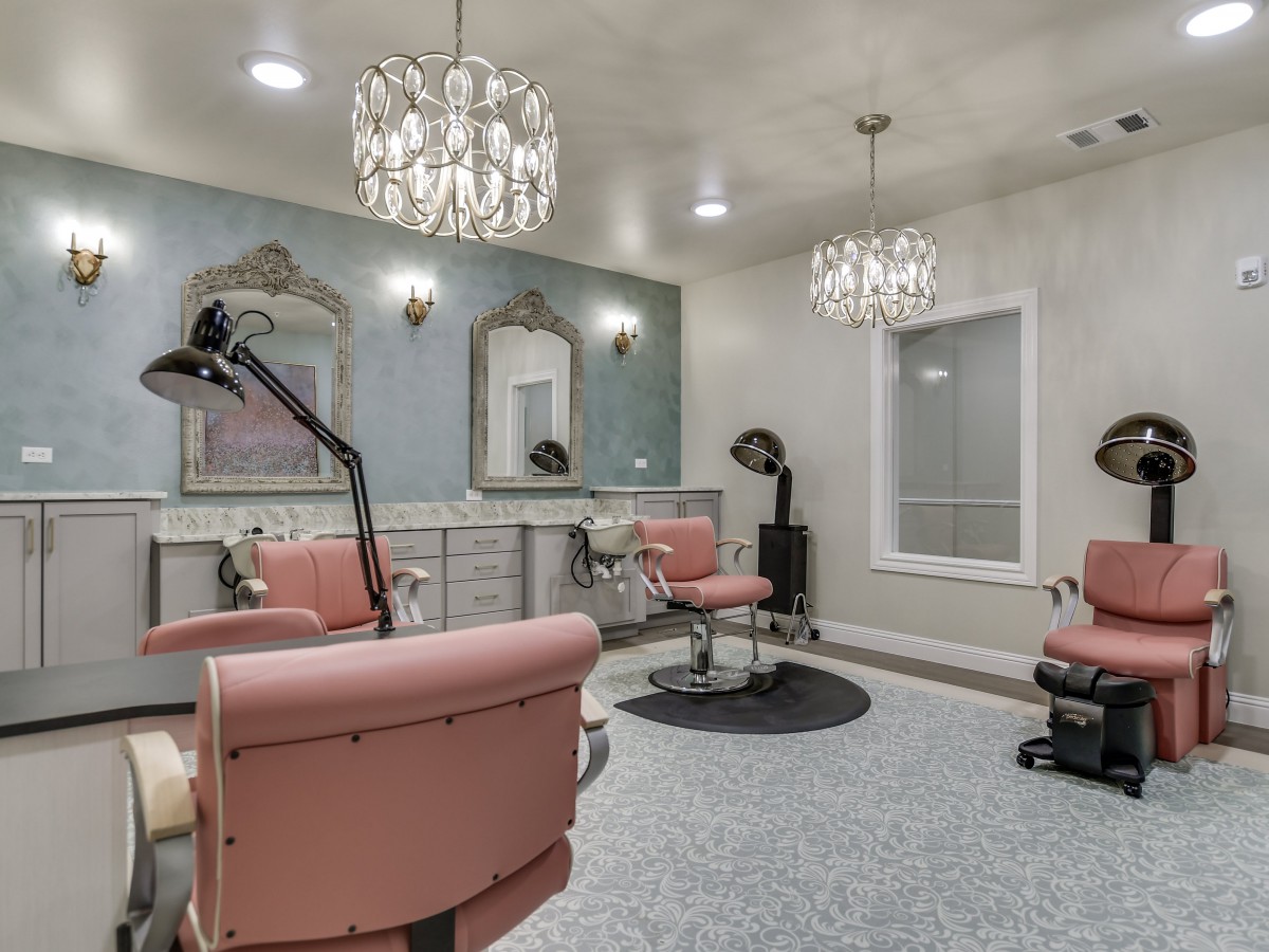 A stylish hair salon with pink chairs and elegant chandeliers.