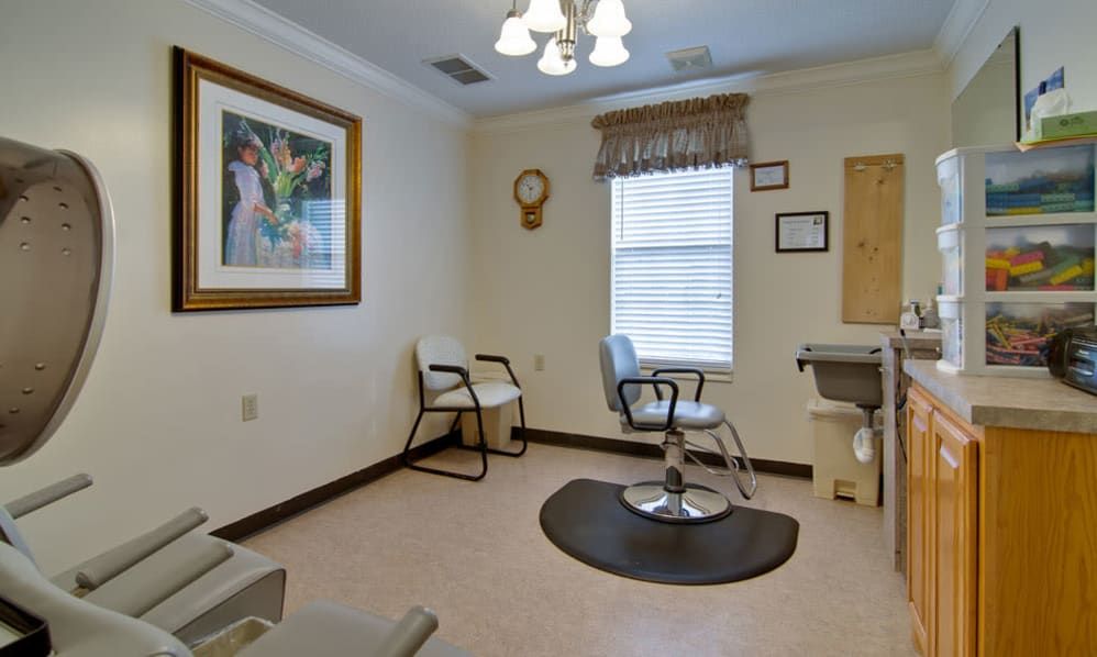 A hair salon interior featuring a single styling chair, a waiting area with chairs, and decorative artwork on the walls.