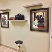 A room interior featuring framed artwork on the wall, a small shelf with items, and a stool beneath.