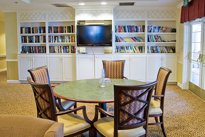 A cozy library room with bookshelves, a round table, chairs, and a television.