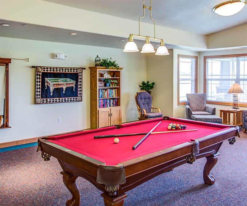 A cozy recreation room featuring a red felt pool table with cues, surrounded by comfortable seating and decor.