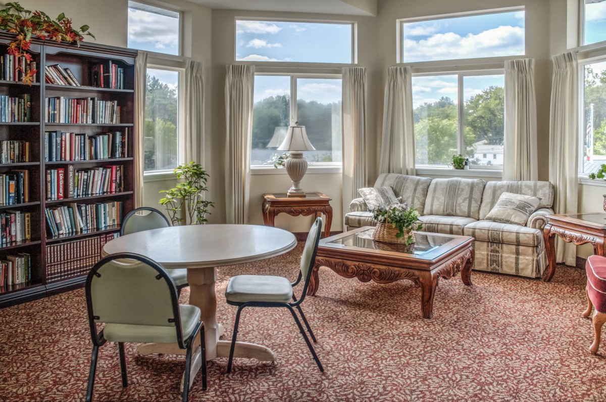 A cozy living room with large windows, a comfortable sofa, and a round table surrounded by chairs.