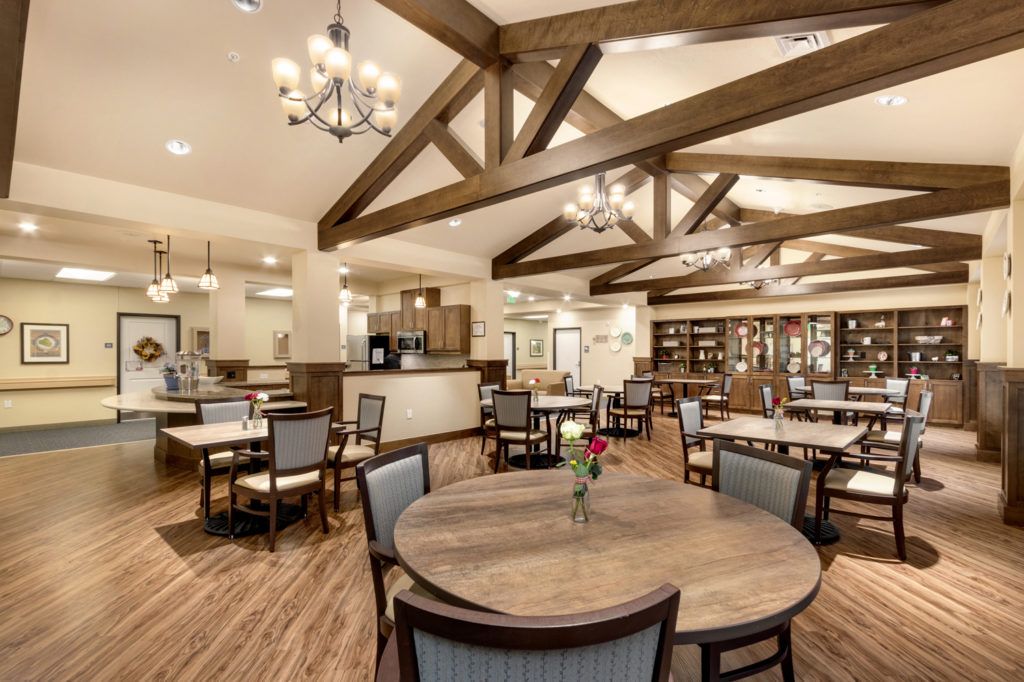 A spacious dining area with wooden tables and chairs, accented by overhead chandeliers and wooden beams.