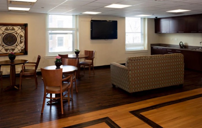 A modern lounge area with a sofa, tables, chairs, and a wall-mounted television.