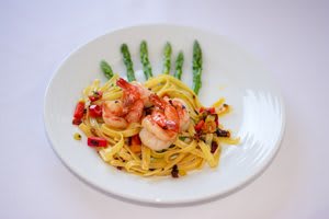 A gourmet dish featuring pasta and shrimp, garnished with asparagus and vegetables.