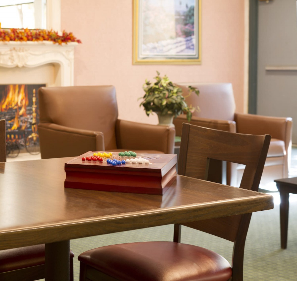 A cozy living room with comfortable chairs, a wooden table, and a warm fireplace.