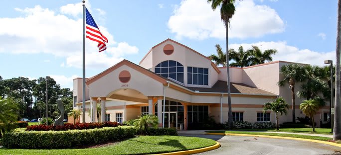 A hospital building with an American flag and palm trees at the entrance on a sunny day.