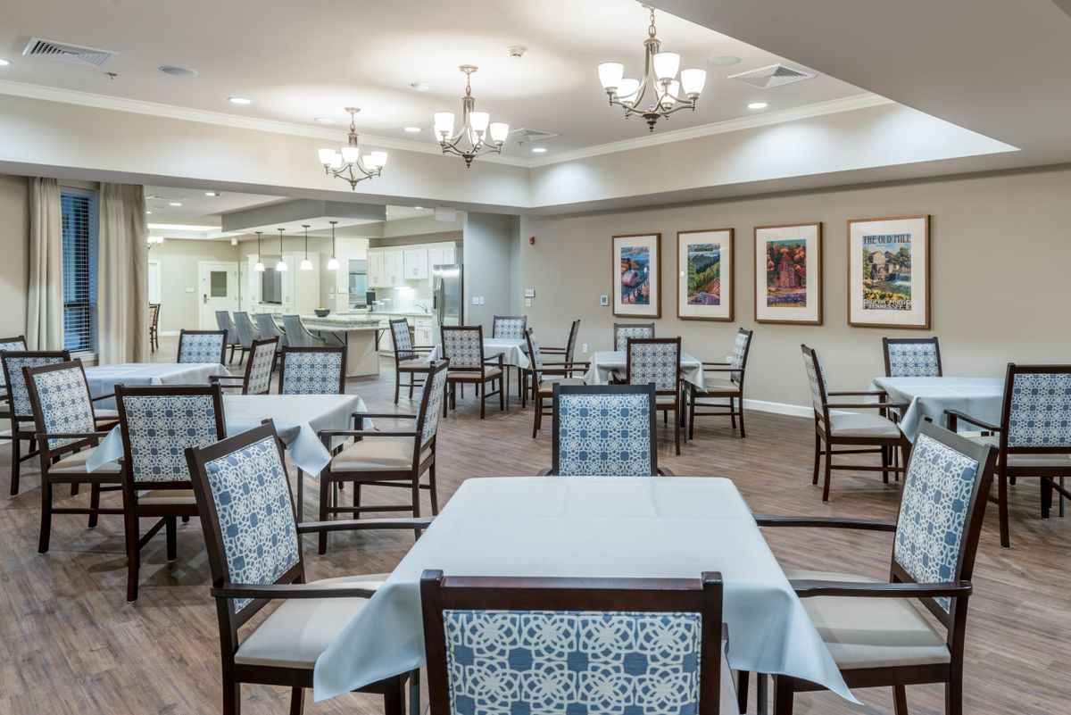 A spacious dining area featuring neatly arranged tables and chairs, illuminated by elegant chandeliers, with artwork adorning the walls.