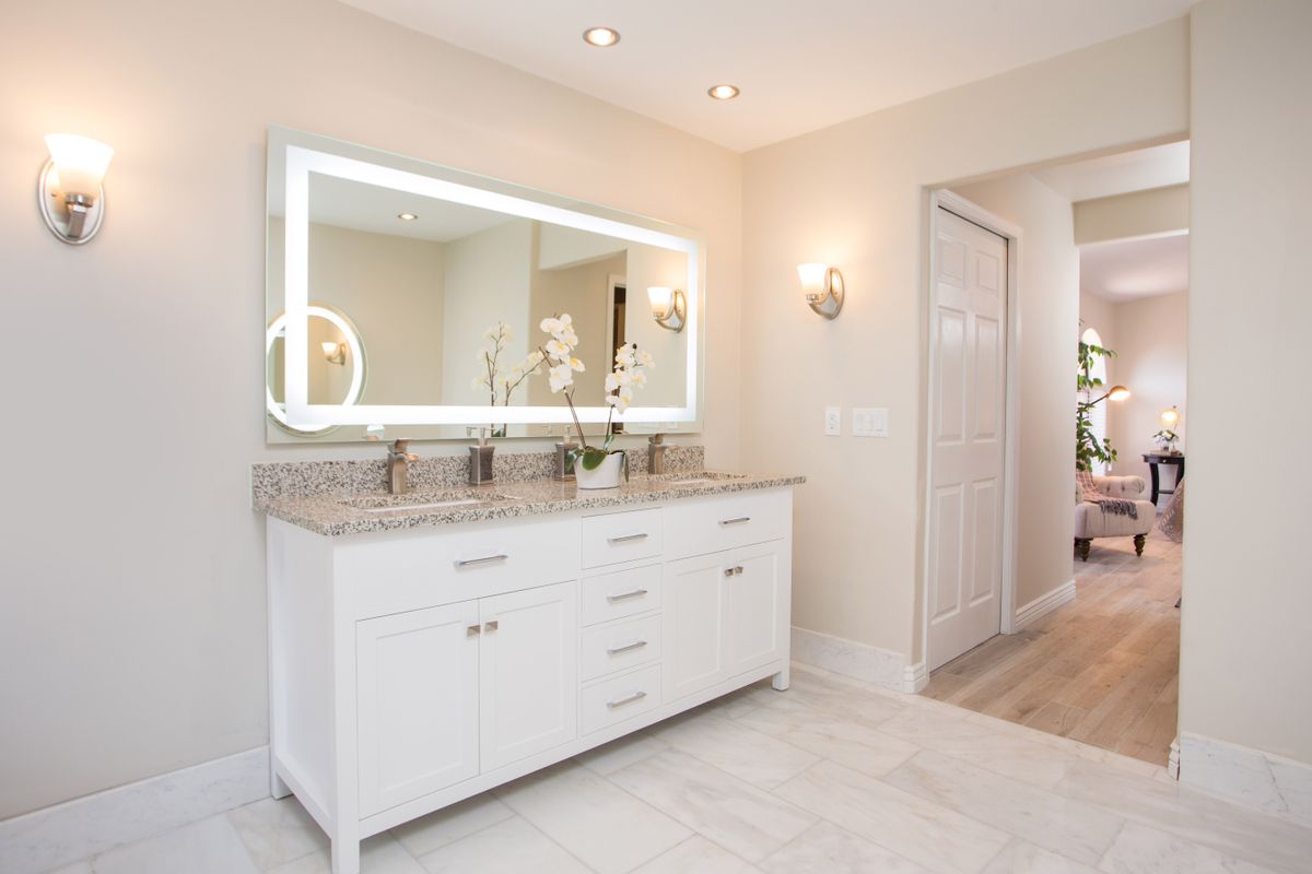A modern bathroom with a large illuminated mirror, white vanity, and elegant lighting.