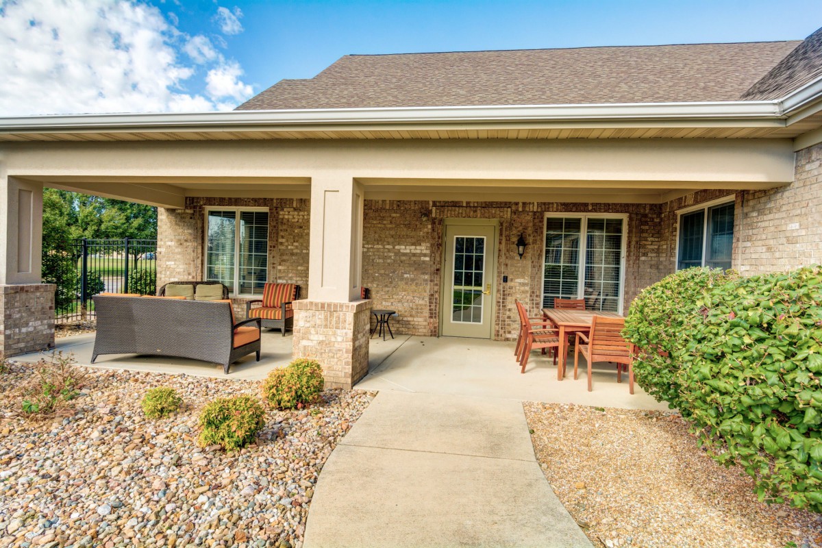A welcoming house with a covered porch and comfortable patio furniture, surrounded by neat landscaping.
