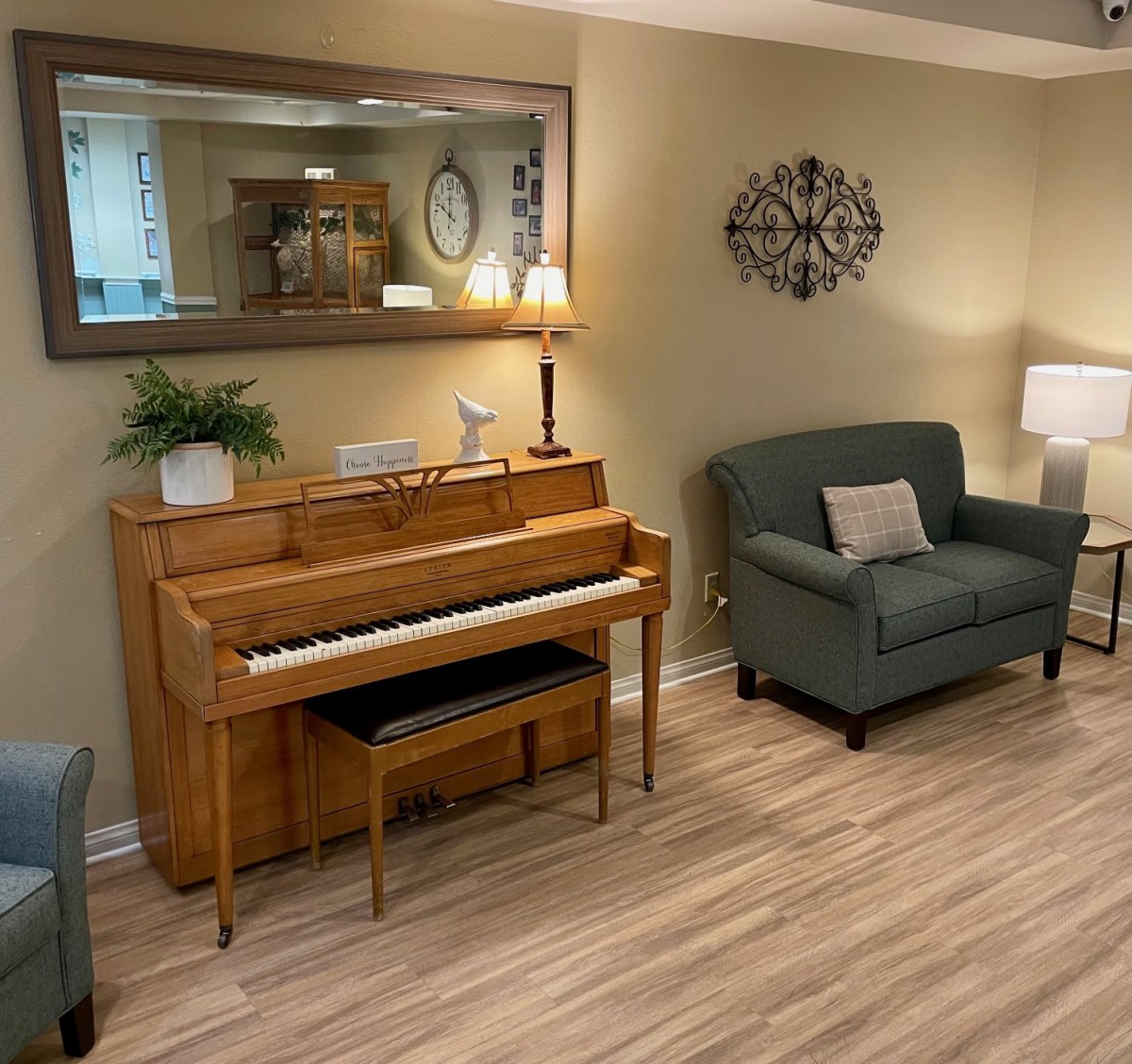 A cozy living room featuring a wooden piano, green armchair, and elegant decor.